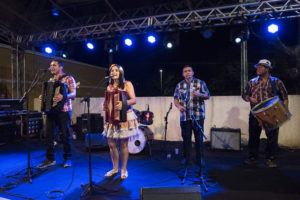 Musical group on stage singing - includes two percussionists and two people playing accordions.