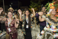 Girl in braids and black dress and woman in red jumpsuit dance smiling with troupe of traditional Brazilian dancers