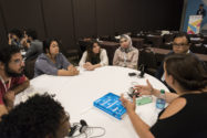 Woman addresses group of people at a round table, discussing urban design